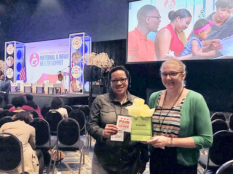 two people at the Maternal & Infant Health Summit holding a gift bag and a sticker that has the paid family leave logo